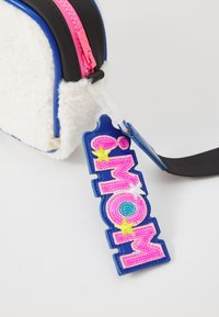 Borsa di materiale bianco peloso con accenti blu e neri, dotata di una cerniera rosa e un vivace portachiavi "MOM" in blu, rosa e giallo.