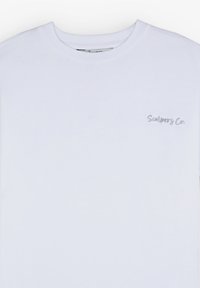T-shirt en coton blanc avec un col rond, présentant un petit texte brodé gris "Scalpers Co." sur la partie gauche de la poitrine. Texture lisse.