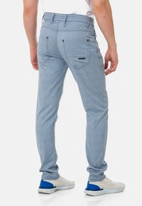 Blaue gestreifte Hose mit Gesäßtaschen, mit schmaler Passform und einem mittelhohen Bund. Kombiniert mit weißen Sneakers und blauen Akzenten.