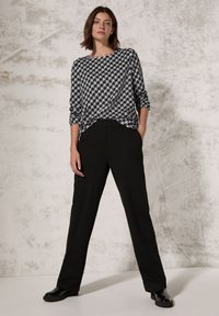 Svart och vit houndstooth-mönstrad topp med lös passform, matchad med svarta rakbenade byxor och blanka svarta skor. Slät textur.