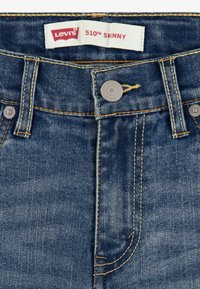 Vaqueros ajustados Levi's 510 en denim azul oscuro, con un diseño clásico de cinco bolsillos, costuras amarillas y cierre de botón metálico.