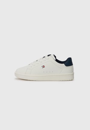 Hvid lav-top sneakers med hvide snørebånd, marineblå hældetalje, lille flaglogo på siden og flad gummisål på grå baggrund.