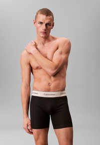 Svarta bomullshorts med en vit Calvin Klein-logo på midjetrimmen, med en fitted design och slät tygkänsla.