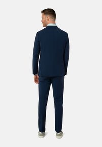 Marineblauer Anzug mit taillierter Passform, einreihiger Jacke und passender Hose. Ausgestattet mit einem hellblauen Kragen und grauen Sneakern.