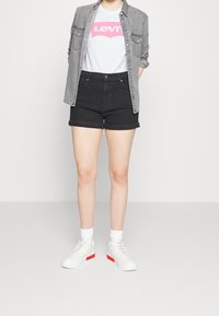 Black denim shorts, light gray button-up shirt, white t-shirt with pink logo, and white sneakers with red accent. Simple, casual outfit.