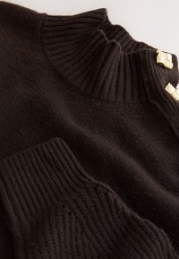 Sort strikket sweater med høj ribstrikket krave, ribstrikkede manchetter og guldfarvede hardware-detaljer. Blød tekstur med en diskret glans.