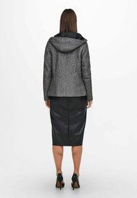 Grå tekstureret frakke med hætte, kombineret med en sort læder pencilskørt. Sættet har et tætsiddende design og elegante sko.