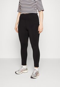 Leggings pretos com uma textura suave, cintura alta e bolso lateral. Combinados com uma blusa cropped às riscas rosa e azul-marinho e sapatilhas prateadas.