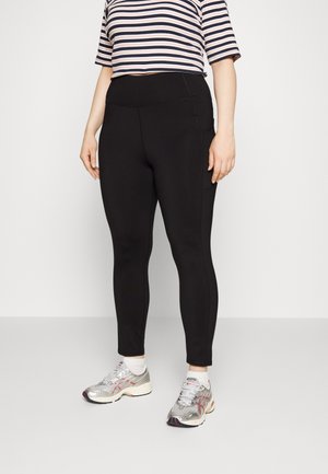 Leggings pretos com uma textura suave, cintura alta e bolso lateral. Combinados com uma blusa cropped às riscas rosa e azul-marinho e sapatilhas prateadas.