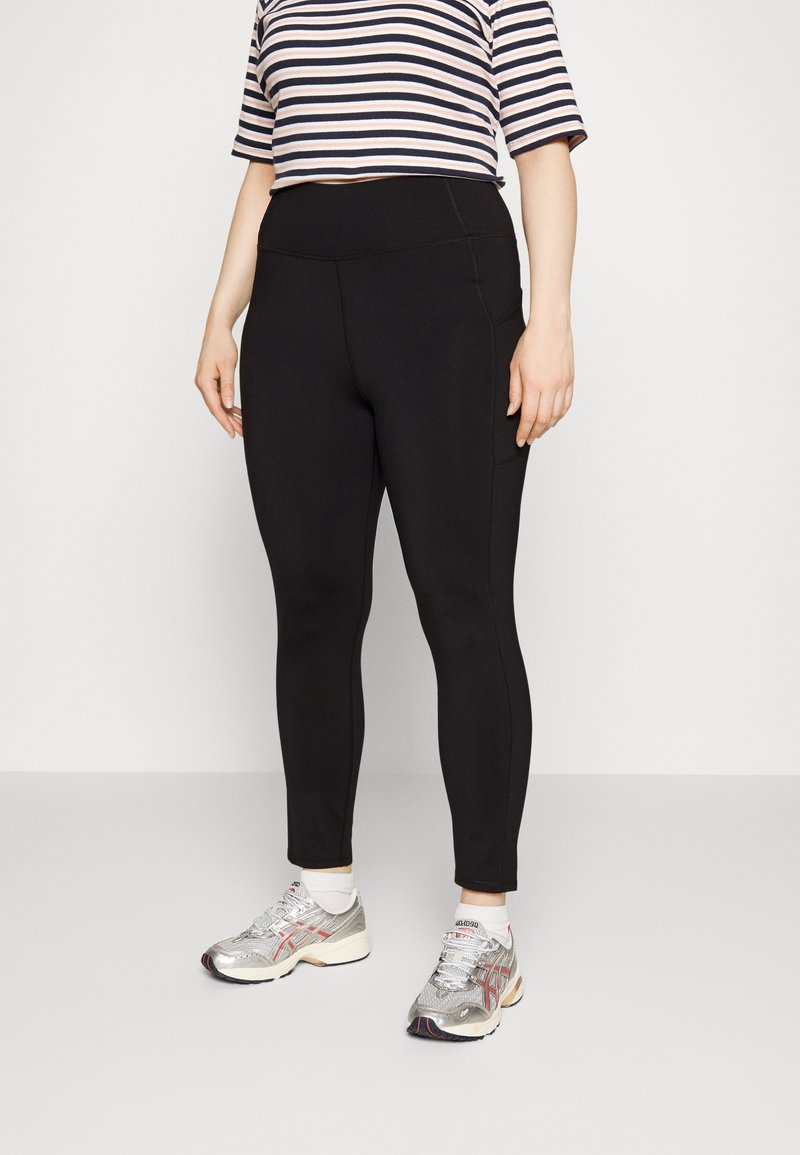 Leggings pretos com uma textura suave, cintura alta e bolso lateral. Combinados com uma blusa cropped às riscas rosa e azul-marinho e sapatilhas prateadas.