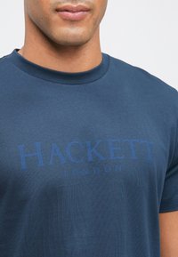 Ναυτικό μπλε βαμβακερό T-shirt με στρογγυλή λαιμόκοψη. Διαθέτει την ένδειξη "HACKETT LONDON" τυπωμένη σε πιο σκούρο μπλε στο στήθος. Λείο υλικό.