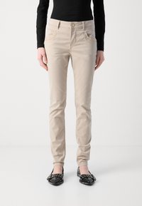 Beige bomullsblandning slim-fit byxor med framfickor, en knappstängning och dekorativ sömnad, kombinerat med svarta platta skor.