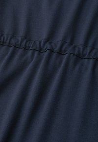Gros plan d’un tissu bleu marine avec une couture élastique froncée créant des plis doux et de la texture.