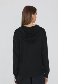 Felpa nera con cappuccio, dal taglio rilassato, maniche lunghe, polsini e orlo a costine. Texture liscia e dettagli di cucitura discreti sulla parte posteriore.