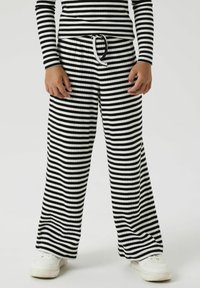Zwart-wit gestreepte wijde broek met ribbelstructuur, voorzien van een elastische tailleband en drawstring. Draagt met witte sneakers.