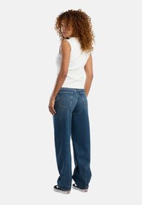 White sleeveless top paired with blue wide-leg jeans. Jeans feature a classic cut with back pockets and subtle stitching detail.