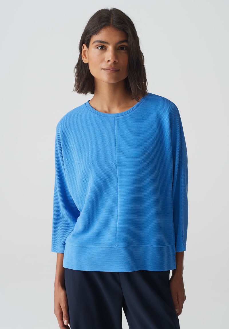 Blauw geribd lang mouwtop met een ronde halslijn en een relaxte pasvorm, met een horizontale textuur en een zijsplit aan de onderkant. Geschikt voor lagen.