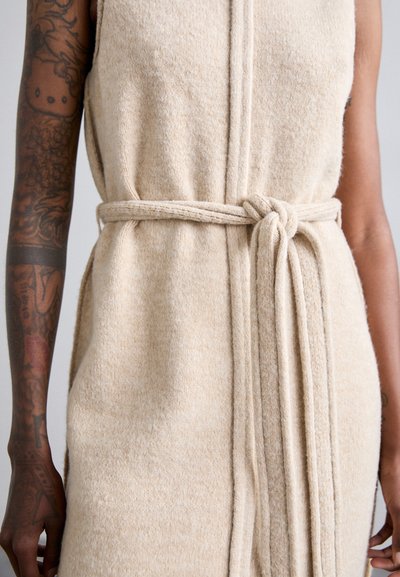 Abito senza maniche beige lavorato a maglia con una cintura in tessuto annodata in vita. La texture è morbida con un motivo sfumato e discreto.