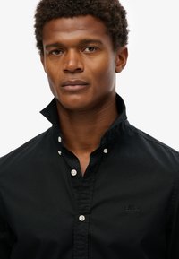 Camisa de botón negra de algodón con cuello clásico, con sutil bordado del logo y un acabado suave y mate.