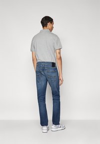 Camisa polo gris combinada con jeans skinny azul oscuro. El denim tiene bolsillos traseros con detalles de costura. Zapatillas blancas completan el conjunto.