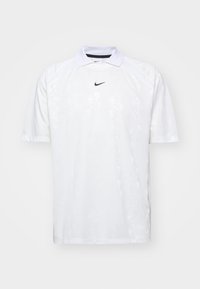 Polo shirt blanc à manches courtes avec col, présentant un motif discret, logo Nike en noir sur la poitrine et texture de tissu douce.