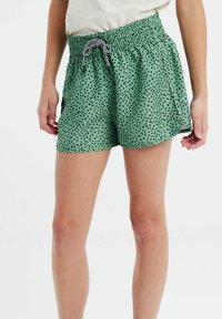 Groene shorts met zwarte stippen, elastische tailleband en trekkoorddetails. Het materiaal lijkt soepel met een lichte, ontspannen pasvorm.