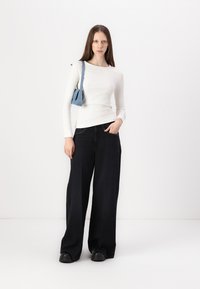 Hvid, ribbet langærmet top parret med brede sorte jeans med nitterlomme. Accessories: lille blå håndtaske. Glat, afslappet look.