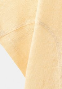 Gros plan sur un tissu en maille beige montrant une texture fine et un détail de couture en courbe sur un matériau textile doux.