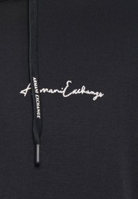 Black hoodie featuring a textured fabric, with a white embroidered logo on the chest and a black drawstring with branding.