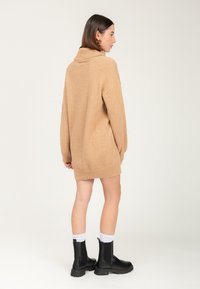 Tan oversized sweater med cowl-neck og ribbede manchetter, parret med sorte ankelstøvler og hvide crew-sokker. Blødt, struktureret strikstof.