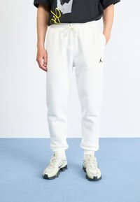 Witte fleece joggingbroek met elastische tailleband en trekkoord, met het zwarte Jordan-logo op de linker bovenbeen. G gedragen met lichte sneakers.