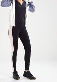 Svarta leggings med en rosa panel och "NIKE AIR" text på sidan, tillsammans med en kortärmad svart topp och svarta sneakers.