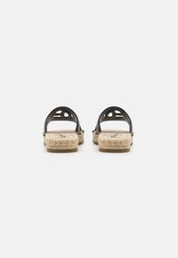 Svarta sandaler med en vävd rep-sula, med utskärning på remmarna och en platt häl. Bakifrån visas designen och texturen.