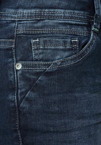 Mörkblå denimjeans med en traditionell femficksdesign, synlig sömnad och en liten metallknapp på bakfickan.