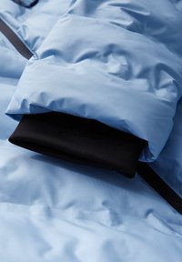 Ljusblå pufferjacka ärm med en svart innermudd. Tyget har en mjuk yta och har quiltade mönster för isolering.