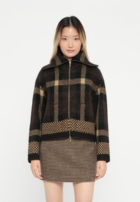 Braun-beige kariertes Zip-Jacke mit hohem Kragen, aus Textilgewebe, kombiniert mit einem passenden Minirock im Hundszahn-Muster.