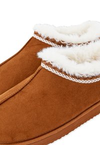 Pantofole in suede marrone con fodera in pelliccia sintetica bianca, bordo intrecciato al polsino e suola in gomma piatta. Texture liscia nel complesso.