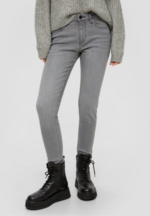 Personne portant un jean skinny gris clair, des bottes de combat à plateforme noires, et un pull en laine gris avec des manches couvrant les poignets.