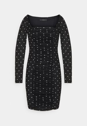 Robe noire à manches longues avec un col carré, un corps froncé et des pois blancs sur toute la surface. Tissu lisse avec une légère transparence au niveau des manches.