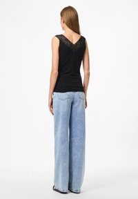 Black sleeveless top with lace trim at the V-neck, paired with light blue wide-leg denim jeans, featuring a frayed hem and minimal detailing.