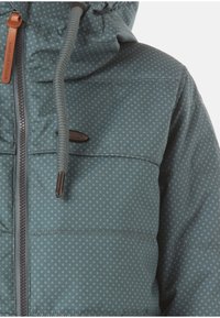 Pěnová bunda v tyrkysové barvě s puntíkovaným vzorem; má přední zip, stahovací kapuci a hn�ědé kožené akcenty. Měkká textura.
