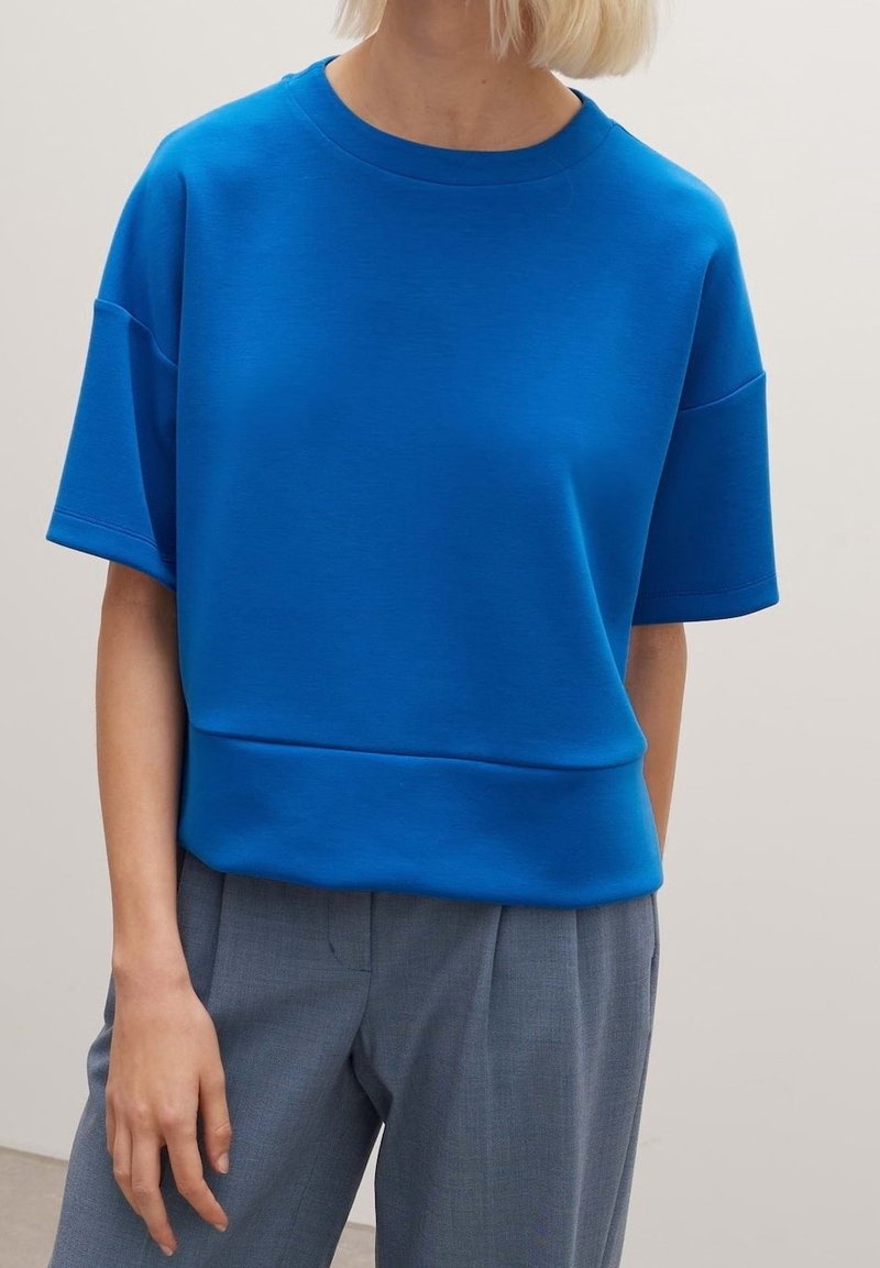 Sweat-shirt bleu en coton avec une coupe décontractée, un col rond et des manches courtes. Associé à un pantalon tailleur gris clair.