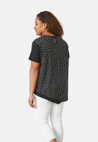 Top a maniche corte bianco e nero a pois con design a occhio di bue sul retro, abbinato a pantaloni bianchi alla caviglia con dettagli a bottoni.