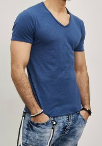 T-shirt bleu à manches courtes et col en V avec une texture douce, présentant une coupe slim et un subtil motif chiné. Porté avec un denim décontracté.