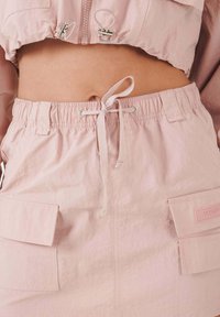 Ljusrosa croppad topp och matchande lösa shorts med elastisk midja, dragsko och framfickor. Slät textur och avslappnad design.