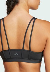 Sostén deportivo negro con tirantes finos, textura suave y acento de marca. Presenta un diseño de espalda estructurada para brindar soporte y estilo.