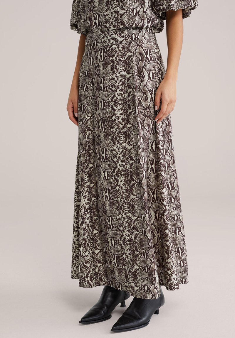 Spódnica maxi w wzór skóry węża, obejmująca odcienie brązu i kremu. Wykonana z lekkiego materiału, zestawiona z czarnymi, szpiczastymi botkami za kostkę.