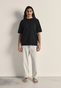 Černé bavlněné tričko s krátkým rukávem, kombinované se světlými rovnými džíny a bílými žabkami. Jednoduchý, uvolněný střih.