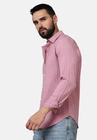 Camicia a maniche lunghe rosa con texture a righe orizzontali, chiusura a bottone e polsini arrotolati. Indossata con jeans casual di un blu chiaro.