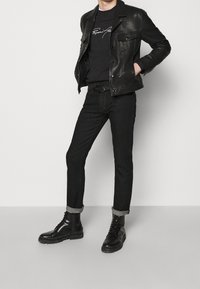 Black leather jacket over a black sweatshirt with white lettering, paired with black jeans and black lace-up boots with a thick sole.